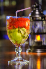 Cocktail drink with strawberries and kiwi fruit on the bar counter with blurred background.