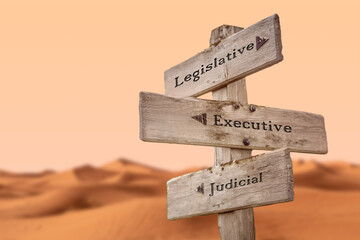 legislative executive judicial text quote on wooden signpost outdoors in dry desert sand dune...