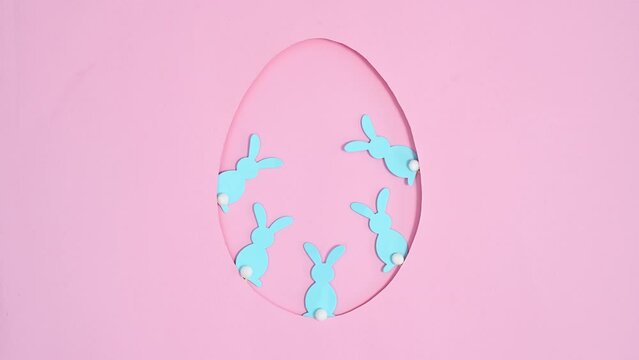 Blue rabbits move in Easter egg shape frame on pastel pink background. Stop motion flat lay