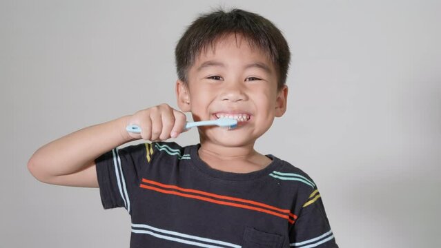 Little cute kid boy 5-6 years old brushing teeth and smile in studio shot isolated on white background, happy Asian children holding toothbrush in mouth by himself, Dental hygiene healthy concept