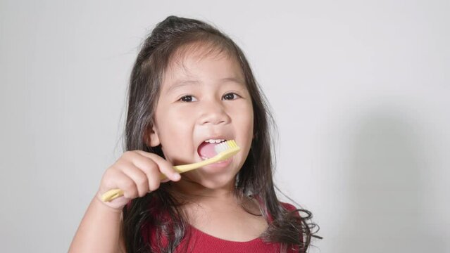 Little cute kid girl 3-4 years old brushing teeth and smile in studio shot isolated on white background, happy Asian children holding toothbrush in mouth by himself, Dental hygiene healthy concept