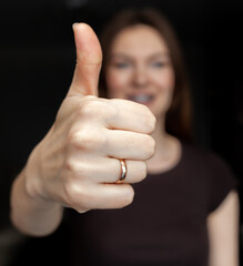 A closeup image of a young woman doing and showing a thumbs-up on a dark background. The concept of success