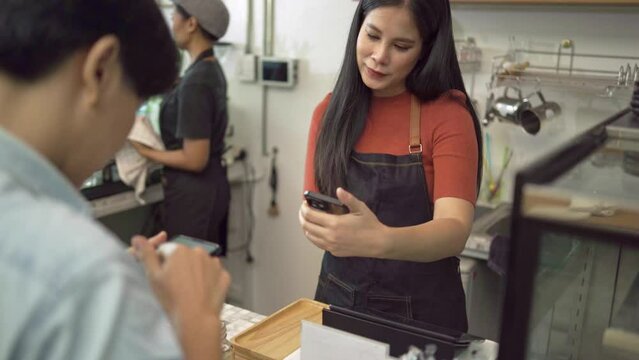 Coffee shop owners accept payments from customers by paying via smartphone, scanning QR Codes instead of cash as contactless payments, and serving coffee to customers in coffee shop concept.