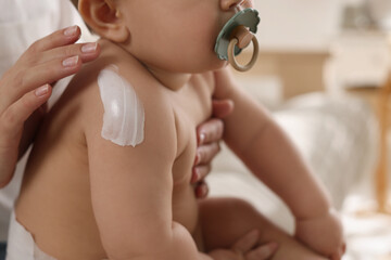 Obraz na płótnie Canvas Mother applying body cream on her little baby at home, closeup