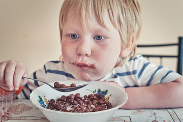 Little boy is having breakfast with chocolate balls with milk - 490828332
