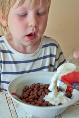 Little boy is having breakfast with chocolate balls with milk - 490828393