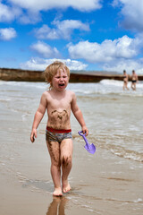 A little boy gets dirty in mud and walks crying along the beach - 490828781