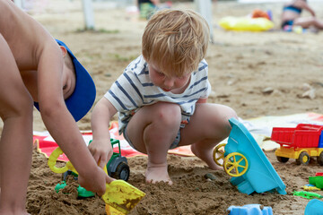 Two children play in the sand with plastic toys - 490828913