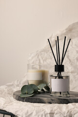 Fototapeta na wymiar Aromatic reed air freshener, eucalyptus leaves and candle on white crumpled paper, space for text