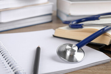 Student textbook, blank notebook, pencil and stethoscope on wooden table, closeup. Medical education
