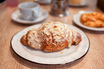 A fresh large croissant on a beautiful plate in a cafe or restaurant. Close-up of a croissant and cream sprinkled with nuts. Sweet and delicious dessert for coffee time.