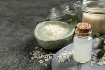 Glass bottle with rice water and grains on grey table. Space for text