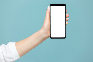 Close-up of a woman's hand with a smartphone on which there is a white screen for advertising, on a blue background. Copy paste.