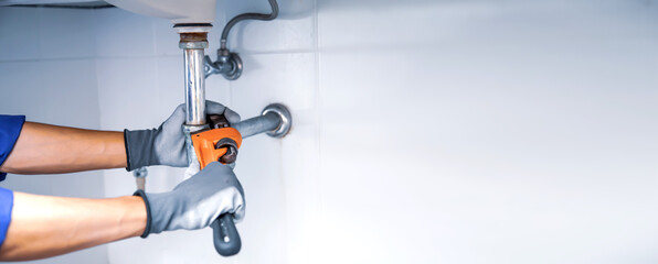 Technician plumber using a wrench to repair a water pipe under the sink. Concept of maintenance,...