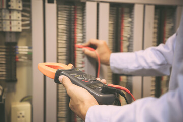 Electricity and electrical maintenance service, Engineer hand holding AC voltmeter checking electric current voltage at circuit breaker terminal and cable wiring main power distribution board.