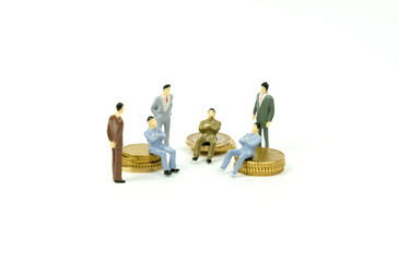 On the white surface on the coins and next to them are miniature figures of businessmen conferring.