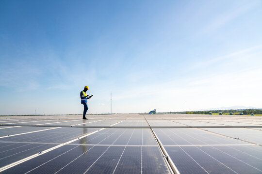 African man engineer using digital tablet maintaining solar cell panels on building rooftop. Technician working outdoor on ecological solar farm construction. Renewable clean energy technology concept