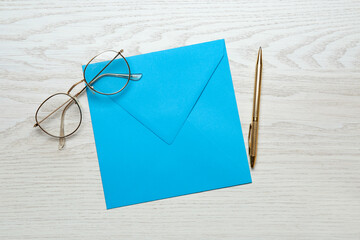 Turquoise envelope, glasses and pen on white wooden table, flat lay
