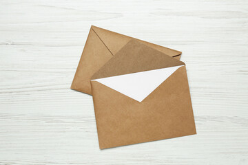 Envelopes with blank paper card on white wooden table, top view
