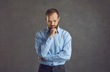 Adult handsome man in casual t-shirt standing over grey background feeling confuse and wonder about question studio portrait headshot. Uncertain with doubt, thinking with hand on head. Pensive concept