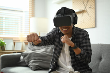 Fototapeta premium Man wearing virtual reality headset playing simulation boxing game in living room.