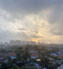 Water drops on window glass with blurred sunset and city buildings as background 