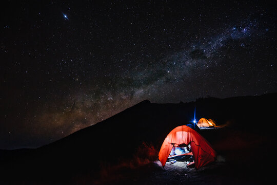 Amazing night scenery with beautiful milky way on the sky with camping tent in the foreground at Senaru Crater Rim, Mount Rinjani Indonesia. (noise grain soft focus visible due to long exposure)