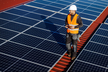 A happy worker walking on the roof with tablet in hands and testing on solar panels.