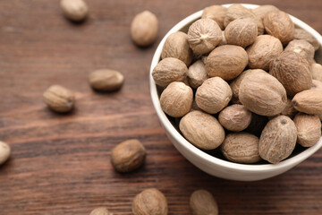 Bowl with nutmeg seeds on wooden table, closeup. Space for text