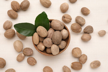 Scattered nutmeg seeds and bowl on white wooden table, flat lay