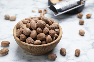 Scattered nutmeg seeds, wooden bowl and grater on white marble table