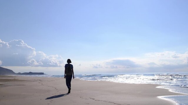 Backpacker female walking on Patara sand dunes beach enjoying windy Mediterranean Sea during Lycian Way trekking back or rear view. Famous Likya Yolu Turkish route. Active people vacation concept