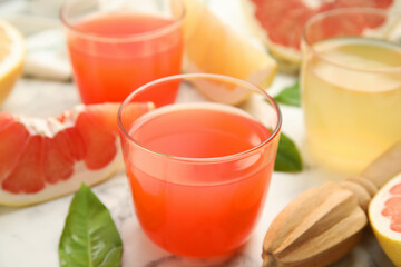 Glass of pink pomelo juice and reamer on white marble table, closeup