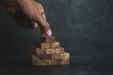 Hand place wooden block stack in pyramid stair step concept of prevent collapse or crash of...