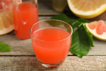 Glass of pink pomelo juice with green leaves on wooden table, closeup