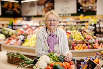 Senior woman purchasing organic vegetables at supermarket and smiling at the camera.