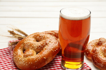 Glass of lager beer with tasty freshly baked pretzels on white table, closeup