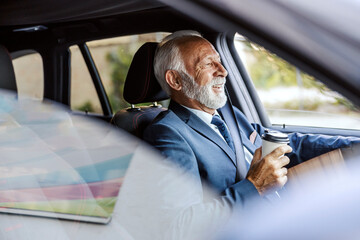 An old businessman driving car to work and drinking a morning coffee to go.