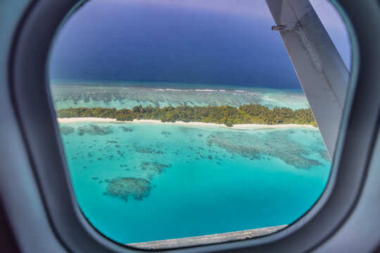 Airplane window with beautiful Maldives island view. Luxury summer holiday travel tourism background, view from airplane window. Atolls and islands with amazing tropical sea © icemanphotos