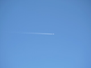 A flying plane leaving a white trail against a blue sky.