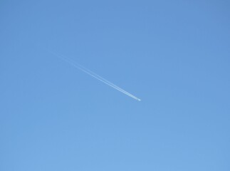 A flying plane leaving a white trail against a blue sky.
