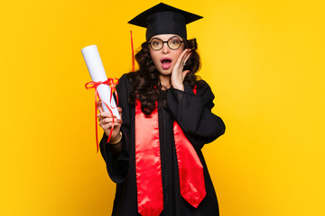 Shocked Girl graduate in graduation hat and eyewear with diploma on yellow backdrop. pleasantly...