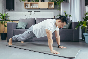 Fototapeta premium Asian performs morning exercises, bar on the floor, male athlete athlete exercises at home, morning workouts