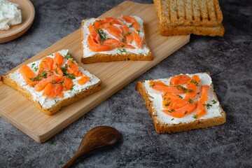 Home made bread on a wooden cutting board with curd cheese, salmon and herbs