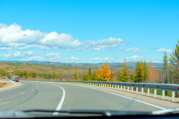 Fototapeta premium Bright autumn scene with road among orange and green trees and blue sky. Soft selective focus. Beauty of nature, travel concept