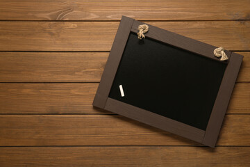 Obraz premium Clean small blackboard with piece of white chalk on wooden table, top view. Space for text