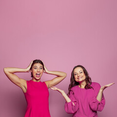 Fototapeta na wymiar Two happy surprised woman laughing, screaming and celebrating success on pink background with copy space for text