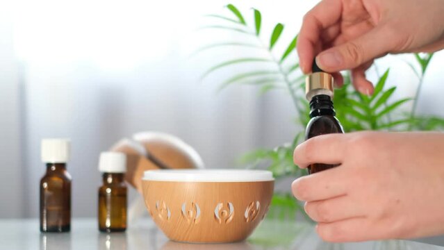 Modern aroma oil diffuser on the white table. Spa concept for body and health care. female is adding essential oil to an aroma diffuser.