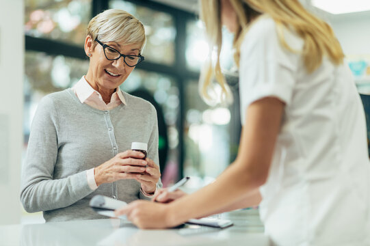Happy senior woman customer buying medications at drugstore while talking with a female pharmacist - Powered by Adobe