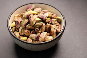 Peeled pistachio nuts in a bowl over black background. Baked pistachios pile, salt pistache, salted pista. Copyspace